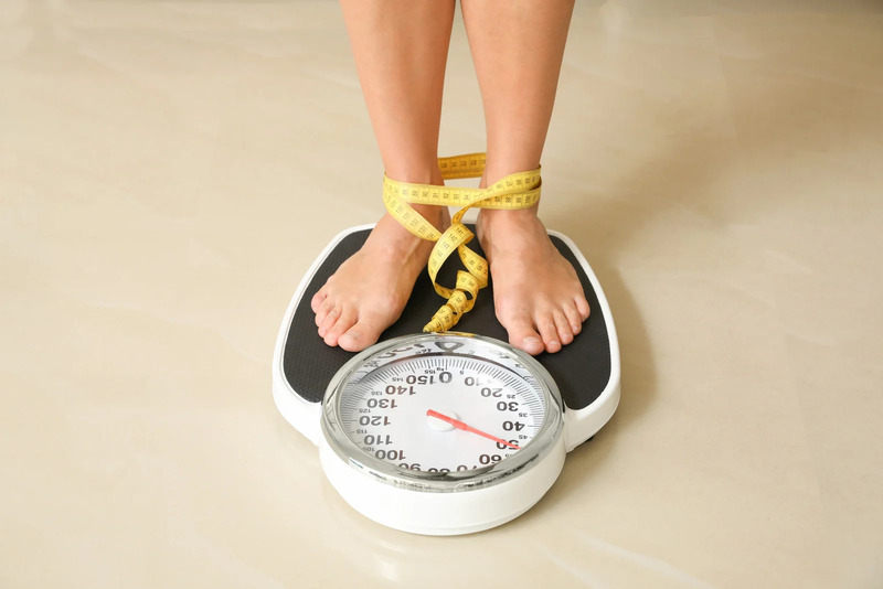 femme montée sur une balance avec un mètre ruban autour des chevilles